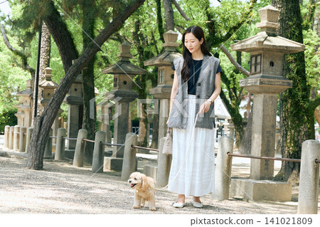 一位女士牽著她的狗沿著通往一座擺滿石燈籠的神社的小路散步。 141021809