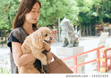 一名女子抱著她的狗,雙手合十在神龕前祈禱。 一名女子抱著她的狗,雙手合十在神龕前祈禱。 141021816