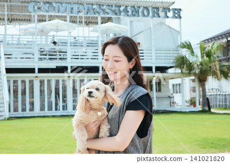 一位面帶微笑的年輕女子抱著她的狗站在一家白色咖啡館前。 141021820