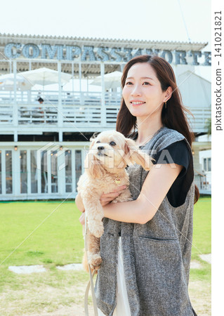A young woman smiling while holding her dog in an outdoor spot with a green lawn. A young woman smiling while holding her dog in an outdoor spot with a green lawn. 141021821