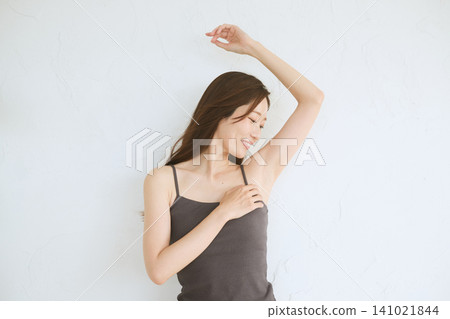 A young woman in a camisole smiles, showing her armpit. A young woman in a camisole smiles, showing her armpit. 141021844