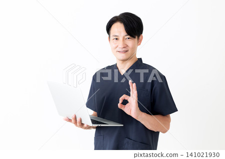 A middle-aged male doctor in navy blue scrubs makes a circular motion while holding a laptop. 141021930