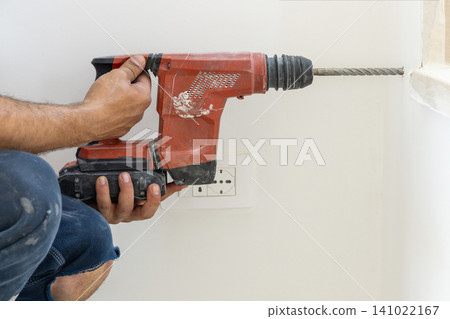 Construction worker drilling hole in concrete wall with cordless rotary hammer, side view 141022167