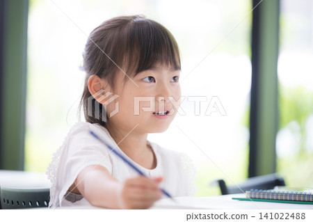 A kindergarten or elementary school girl concentrating on studying while looking at the blackboard in the classroom; attending cram school or regular school; preparing for exams or studying. A kindergarten or elementary school girl concentrating on studying while looking at the blackboard in the classroom; attending cram school or regular school; preparing for exams or studying. 141022488