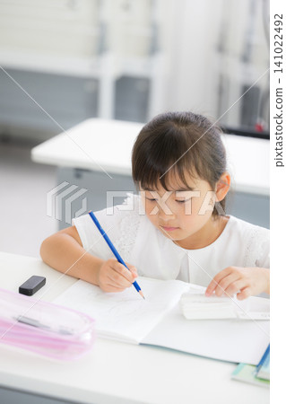 一個大約小學年齡的小女孩正在專心做數學練習;畫面展現了補習班、正規學校或獨立學習的場景。 一個大約小學年齡的小女孩正在專心做數學練習;畫面展現了補習班、正規學校或獨立學習的場景。 141022492