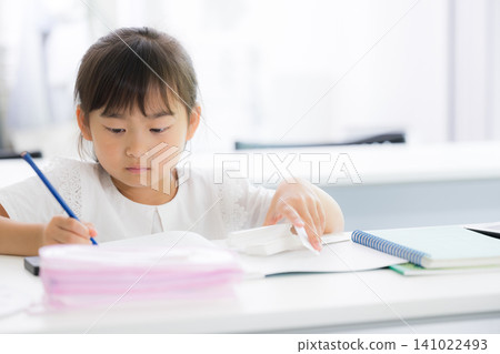 A kindergarten or elementary school-aged girl concentrating on math drills in a classroom; an image of a cram school, regular school, exams, studying, and learning. A kindergarten or elementary school-aged girl concentrating on math drills in a classroom; an image of a cram school, regular school, exams, studying, and learning. 141022493