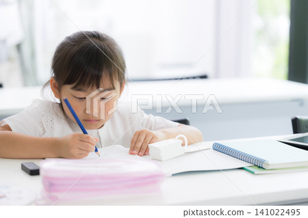 一個幼稚園或小學年齡的女孩在教室裡專心做數學練習;補習班、正規學校、考試、學習的畫面。 一個幼稚園或小學年齡的女孩在教室裡專心做數學練習;補習班、正規學校、考試、學習的畫面。 141022495