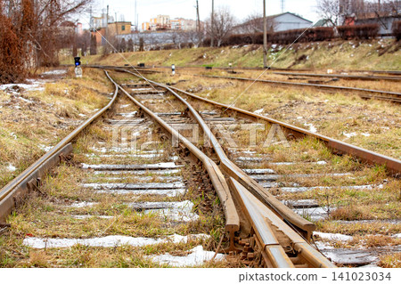 Train tracks run through a grassy area with signs and buildings visible in the background on a cloudy day Train tracks run through a grassy area with signs and buildings visible in the background on a cloudy day 141023034