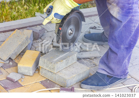 Person cuts stones using a power tool for paving work in a garden during the day Person cuts stones using a power tool for paving work in a garden during the day 141023037