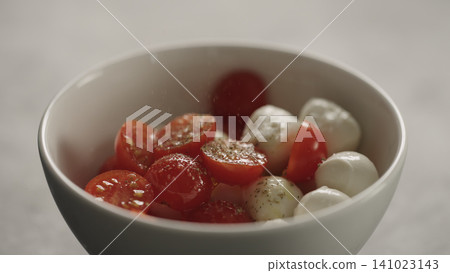 making salad with mozzarella and cherry tomatoes, caprese style in white bowl closeup making salad with mozzarella and cherry tomatoes, caprese style in white bowl closeup 141023143