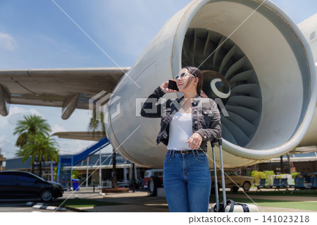 Asian woman talking on smartphone next to airplane jet engine for travel transit Asian woman talking on smartphone next to airplane jet engine for travel transit 141023218