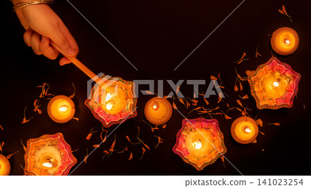 Hand lighting clay diya oil lamp for Diwali festival celebration Hand lighting clay diya oil lamp for Diwali festival celebration 141023254
