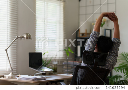 Man stretching arms overhead at desk for workplace wellness and stress relief Man stretching arms overhead at desk for workplace wellness and stress relief 141023294