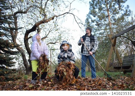 Young father, pre-teen daughter and son in warm autumn clothes spending quality time together among fallen leaves. Happy family enjoying the beauty of fall, playful moments and family life outdoors Young father, pre-teen daughter and son in warm autumn clothes spending quality time together among fallen leaves. Happy family enjoying the beauty of fall, playful moments and family life outdoors 141023531