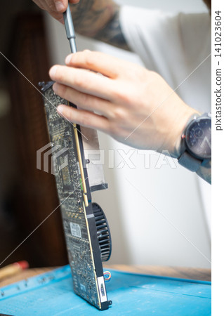 Person repairs a computer graphics card in a workshop during the day using tools for maintenance and improvement Person repairs a computer graphics card in a workshop during the day using tools for maintenance and improvement 141023604
