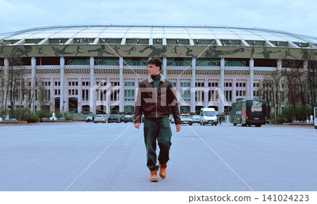 Teenager Walking Confidently Near Large Stadium Building Teenager Walking Confidently Near Large Stadium Building 141024223