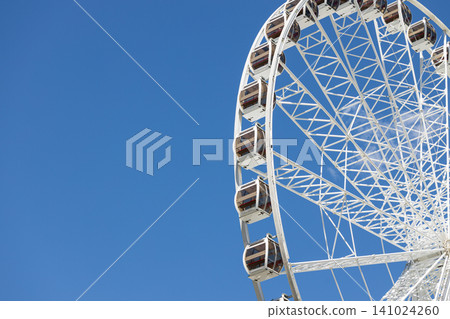 Giant Ferris wheel with cabins against a clear blue sky on a sunny day Giant Ferris wheel with cabins against a clear blue sky on a sunny day 141024260