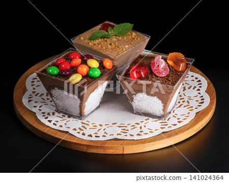Close-up: three chocolate dessert cups filled with fresh strawberries and garnished with mint, on a decorative wooden plate. Black background Close-up: three chocolate dessert cups filled with fresh strawberries and garnished with mint, on a decorative wooden plate. Black background 141024364