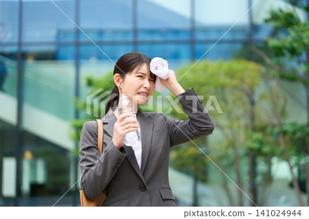 A businesswoman wiping sweat from her brow in the hot outdoors. A businesswoman wiping sweat from her brow in the hot outdoors. 141024944
