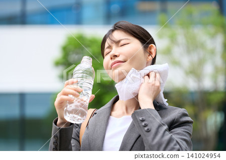 A businesswoman wiping sweat from her brow in the hot outdoors. A businesswoman wiping sweat from her brow in the hot outdoors. 141024954