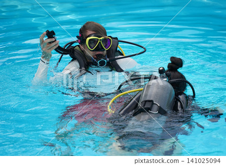 A professional diver and a novice practice diving in a pool. 141025094