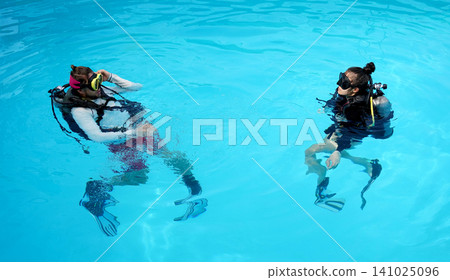 A professional diver and a novice practice diving in a pool. A professional diver and a novice practice diving in a pool. 141025096