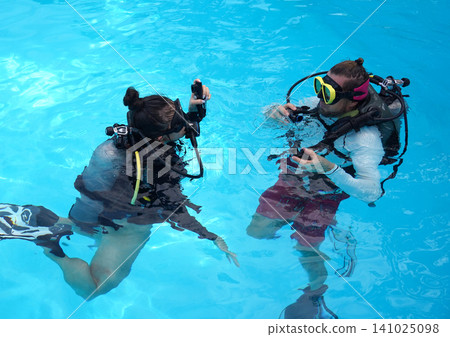 A professional diver and a novice practice diving in a pool. A professional diver and a novice practice diving in a pool. 141025098
