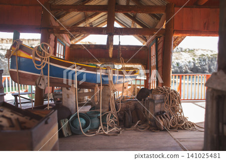 Traditional Maltese fishing boat Luzzu in a rustic wooden boathouse Traditional Maltese fishing boat Luzzu in a rustic wooden boathouse 141025481
