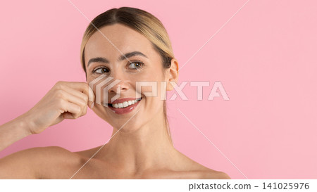 Smiling young woman pinching her cheek playfully, showcasing firm smooth skin Smiling young woman pinching her cheek playfully, showcasing firm smooth skin 141025976