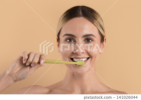Smiling young woman brushing her teeth with green toothbrush, demonstrating dental hygiene Smiling young woman brushing her teeth with green toothbrush, demonstrating dental hygiene 141026044