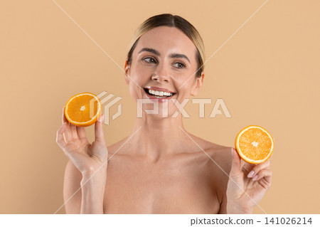 Young beautiful woman smiling while holding fresh orange halves on beige background Young beautiful woman smiling while holding fresh orange halves on beige background 141026214