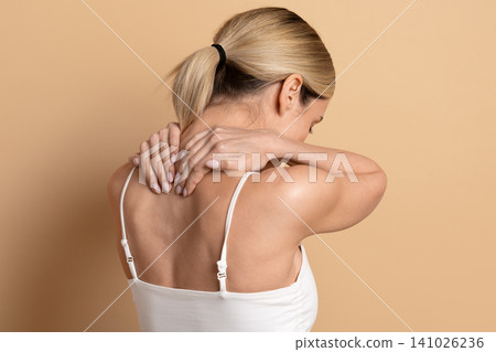 Young beautiful woman massaging her neck and upper back on beige background Young beautiful woman massaging her neck and upper back on beige background 141026236