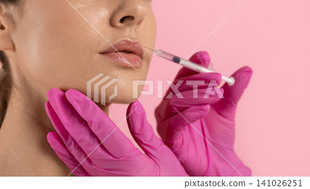 Closeup of womans lips receiving filler injection from gloved hands holding syringe Closeup of womans lips receiving filler injection from gloved hands holding syringe 141026251