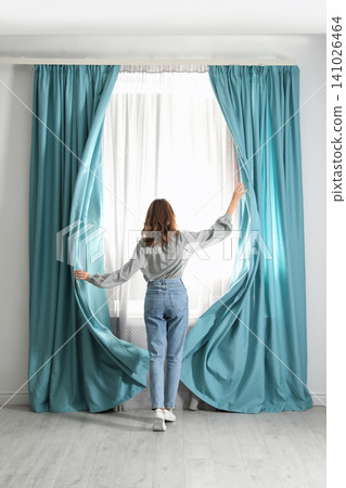 Woman opening window curtains at home in morning, back view Woman opening window curtains at home in morning, back view 141026464