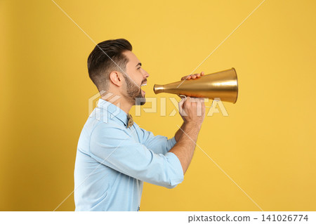 Young man with megaphone on yellow background Young man with megaphone on yellow background 141026774