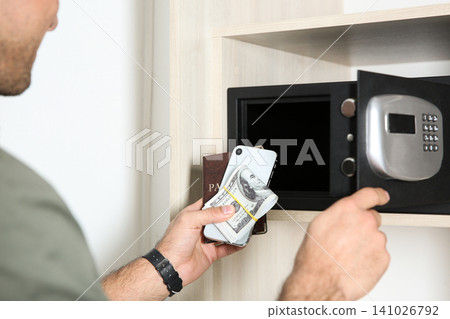 Man putting smartphone, passport and money into steel safe, closeup Man putting smartphone, passport and money into steel safe, closeup 141026792