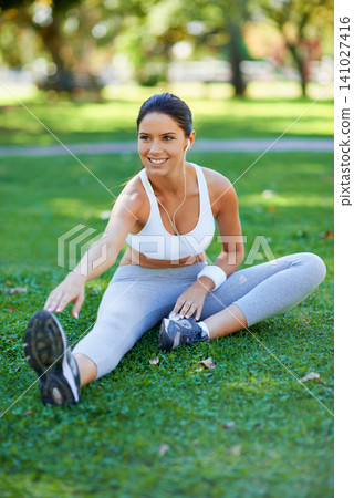 Woman, runner and stretching in nature with earphones for music, fitness and ready for cardio in park. Warm up in grass, start run and listening to radio, sport and flexibility outdoor for exercise Woman, runner and stretching in nature with earphones for music, fitness and ready for cardio in park. Warm up in grass, start run and listening to radio, sport and flexibility outdoor for exercise 141027416