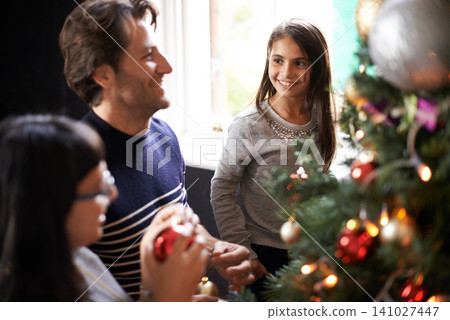 Mom, child and dad at tree for Christmas decoration, bonding and fun in family home. Festive, xmas decor and mother with girl kid, father and happy holiday together in support, love and celebration. Mom, child and dad at tree for Christmas decoration, bonding and fun in family home. Festive, xmas decor and mother with girl kid, father and happy holiday together in support, love and celebration. 141027447