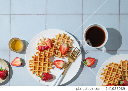 Belgian waffles with fresh strawberries and honey on a white plate on a blue tile background Belgian waffles with fresh strawberries and honey on a white plate on a blue tile background 141028089