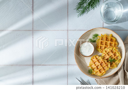 Vegetarian potato waffles with natural yogurt and dill on a plate on a tile background Vegetarian potato waffles with natural yogurt and dill on a plate on a tile background 141028210