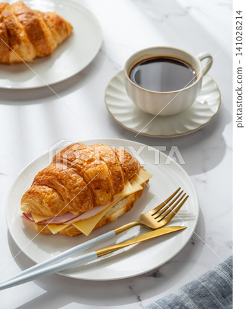 A golden croissant sandwich with ham and cheese on a white plate on a marble background 141028214