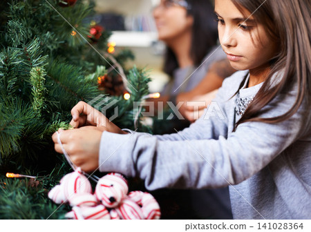 Decoration, child and ornament by Christmas tree in home, festive season and object to prepare for xmas. Female person, girl and care on religious holiday, celebrate and event or party for tradition Decoration, child and ornament by Christmas tree in home, festive season and object to prepare for xmas. Female person, girl and care on religious holiday, celebrate and event or party for tradition 141028364