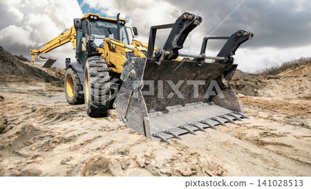 A universal excavator loader is moving dirt at a construction site. The sky is cloudy, and the loader is preparing the ground for building activities A universal excavator loader is moving dirt at a construction site. The sky is cloudy, and the loader is preparing the ground for building activities 141028513