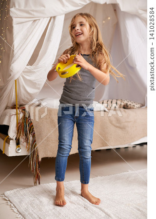 Girl, child and happy in home with tambourine for playing, music or learning rhythm in bedroom. Kid, instrument and smile for noise, sound and laughing for funny games with creativity at family house 141028584