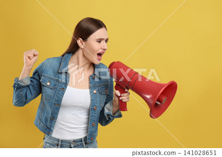 Emotional young woman with megaphone on yellow background Emotional young woman with megaphone on yellow background 141028651
