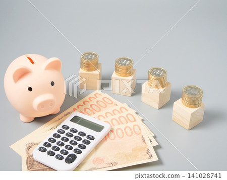An image illustrating wealth building, household budget management, and investment using stacked coins, a calculator, banknotes, and wooden blocks (gray background, copy). 141028741