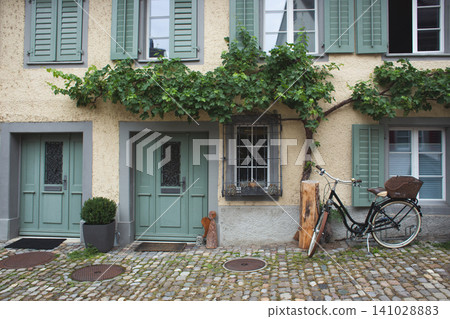 Cozy traditional house facade with green shutters and vintage bicycle 141028883