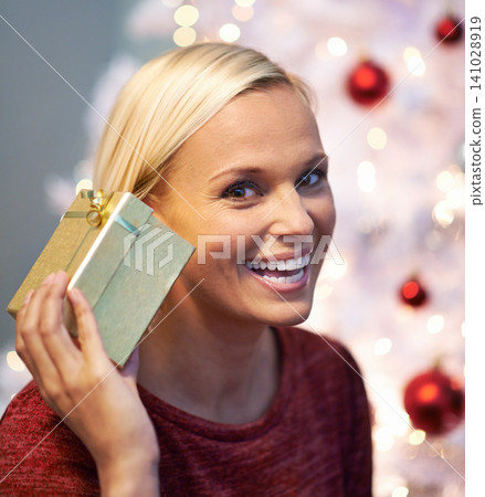 Christmas, gift and excited woman listening with holiday surprise, celebration and tradition at night. Portrait of a young person by tree and bokeh lights with present, box and thanksgiving at home 141028919