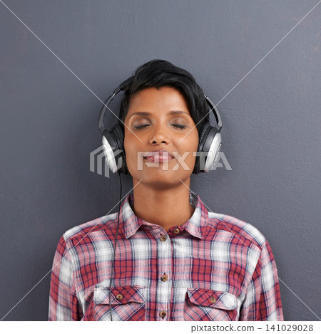 Woman, relax and listening with headphones for music or podcast on a gray studio background. Calm, young female person or Indian with smile or enjoying audio sound track with headset on mockup space Woman, relax and listening with headphones for music or podcast on a gray studio background. Calm, young female person or Indian with smile or enjoying audio sound track with headset on mockup space 141029028