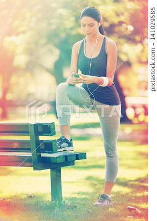 Woman, exercise and listening to music in park, fitness and commitment or training for healthy body. Young lady, smartphone and runner with streaming audio, technology and morning workout in nature Woman, exercise and listening to music in park, fitness and commitment or training for healthy body. Young lady, smartphone and runner with streaming audio, technology and morning workout in nature 141029588